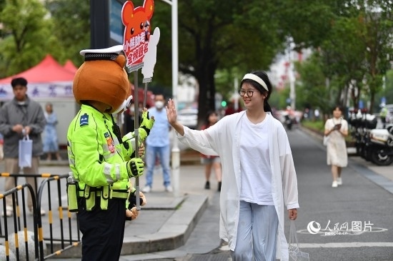6月7日上午9時(shí)，隨著鈴聲的響起，2023年江西高考正式開考，江西省的53.57萬考生以縣（區(qū)）為單位隨機(jī)安排在全省256個考點(diǎn)、18968個考場參加高考。圖為“小熊交警”和考生擊掌鼓勵。 人民網(wǎng)記者 時(shí)雨攝