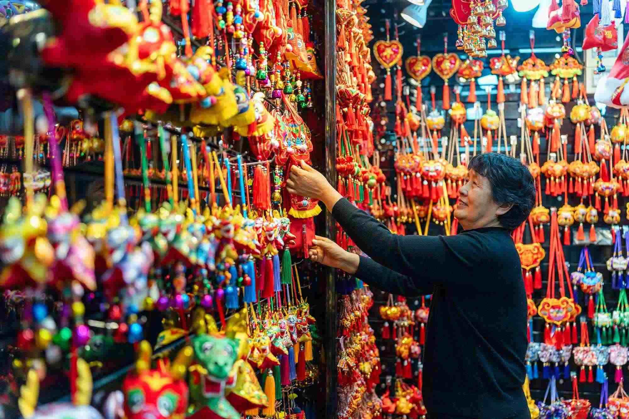 2023年12月11日，金華義烏國際商貿(mào)城，龍年喜慶用品掛滿攤位，顧客正在挑選中。