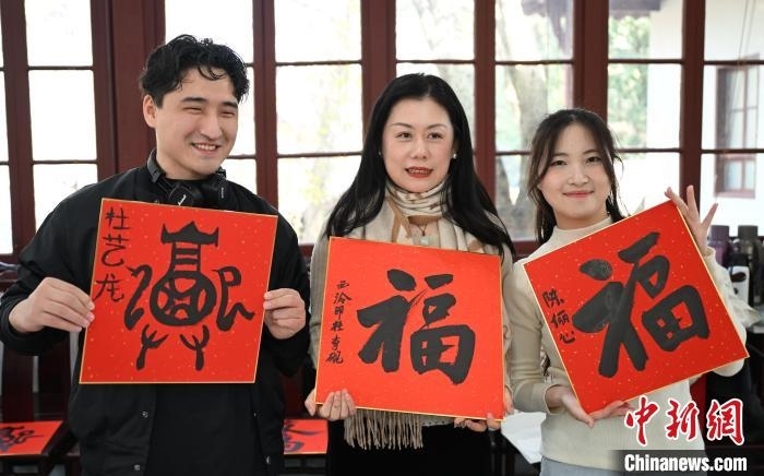 1月20日，外籍留學(xué)生和西泠印社社員李硯(中)展示各自創(chuàng)作的福貼。當(dāng)日，來(lái)自巴西、馬來(lái)西亞、加納、哈薩克斯坦的外籍留學(xué)生在浙江杭州西泠印社體驗(yàn)福貼、春聯(lián)和篆刻，感受古老的中國(guó)傳統(tǒng)文化。中新社記者 王剛 攝